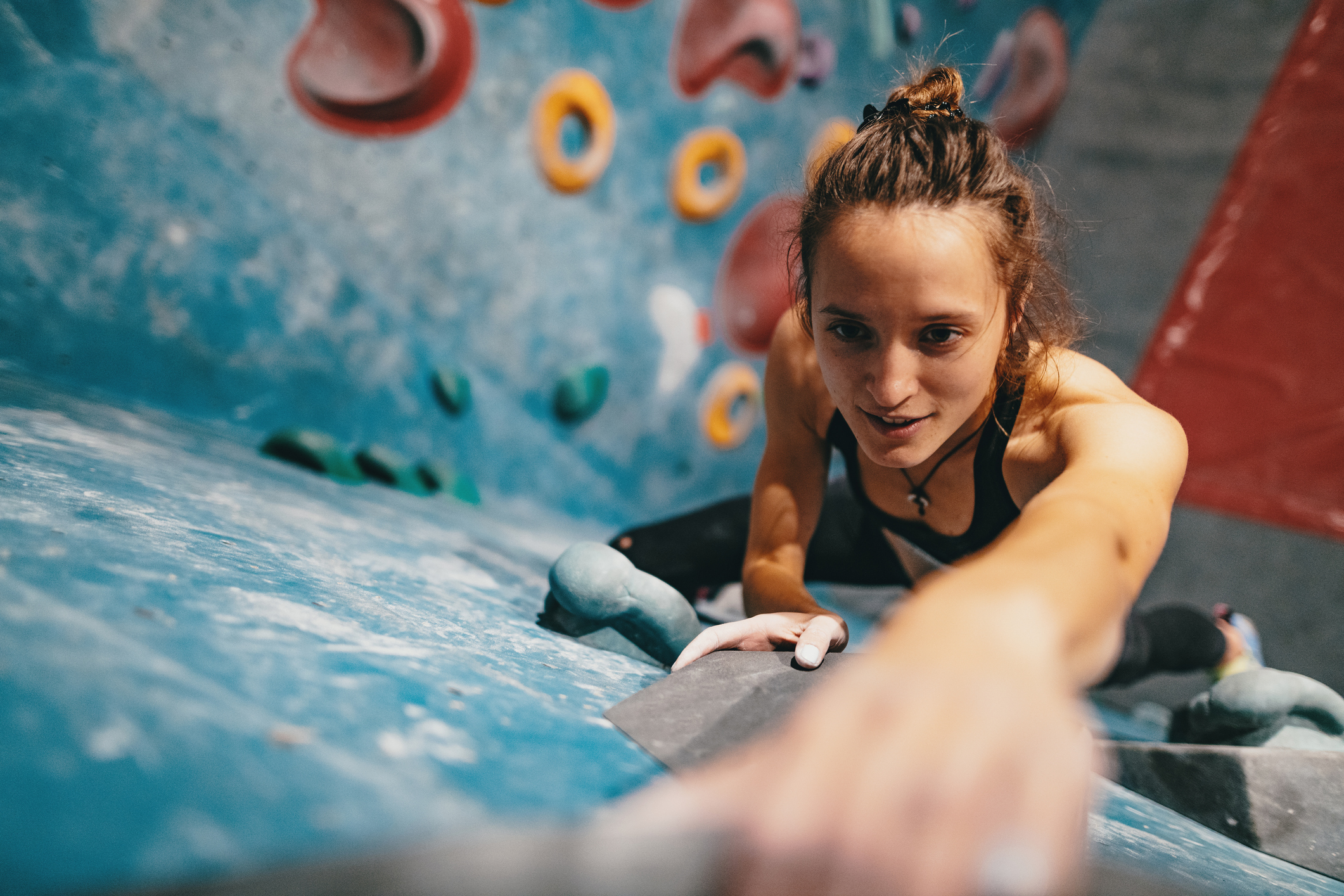 Eine Frau beim Bouldern an einer Kletterwand mit bunten Griffen.