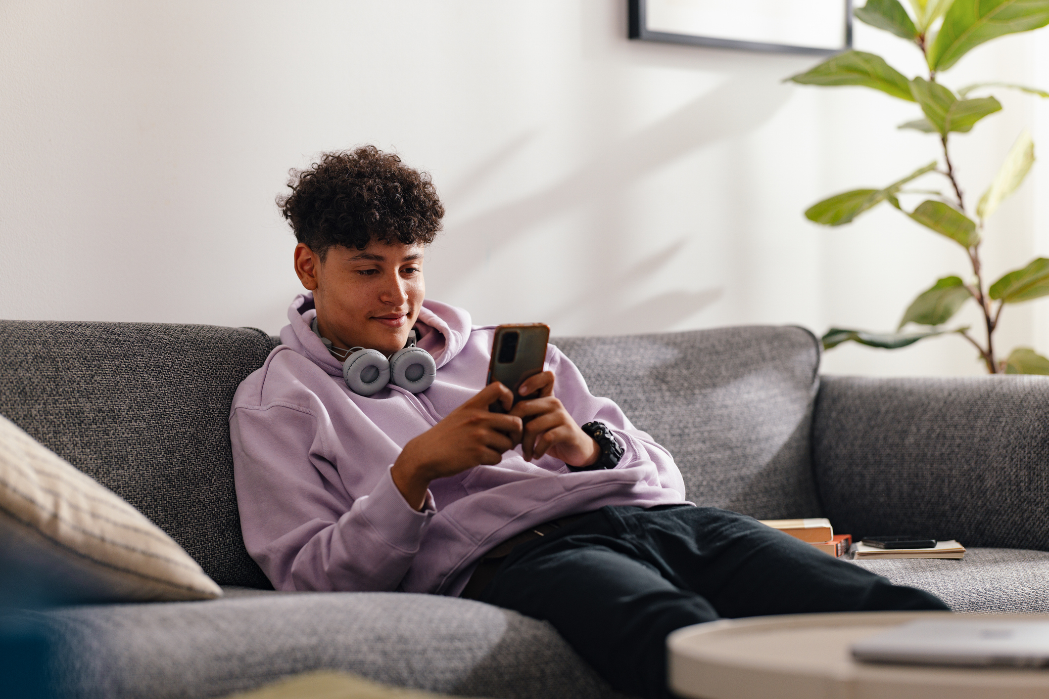 Ein Junge sitzt entspannt auf einem Sofa und schaut lächelnd in sein Smartphone