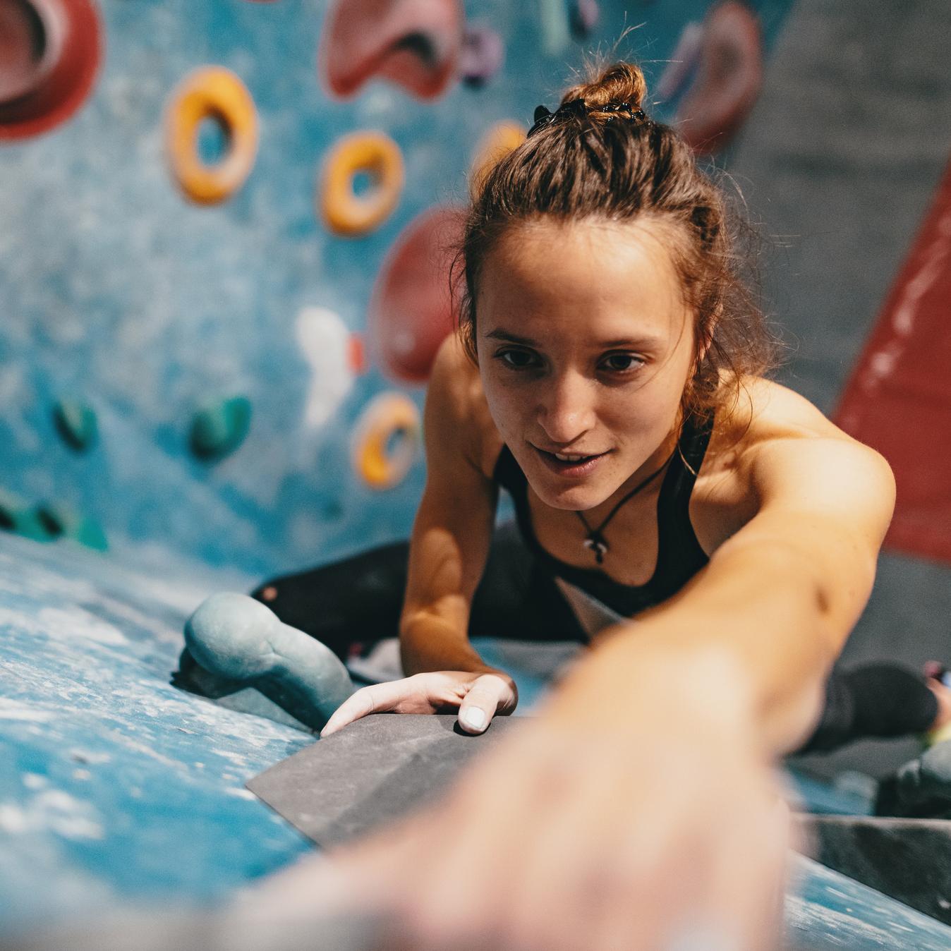 Eine Frau beim Bouldern an einer Kletterwand mit bunten Griffen.