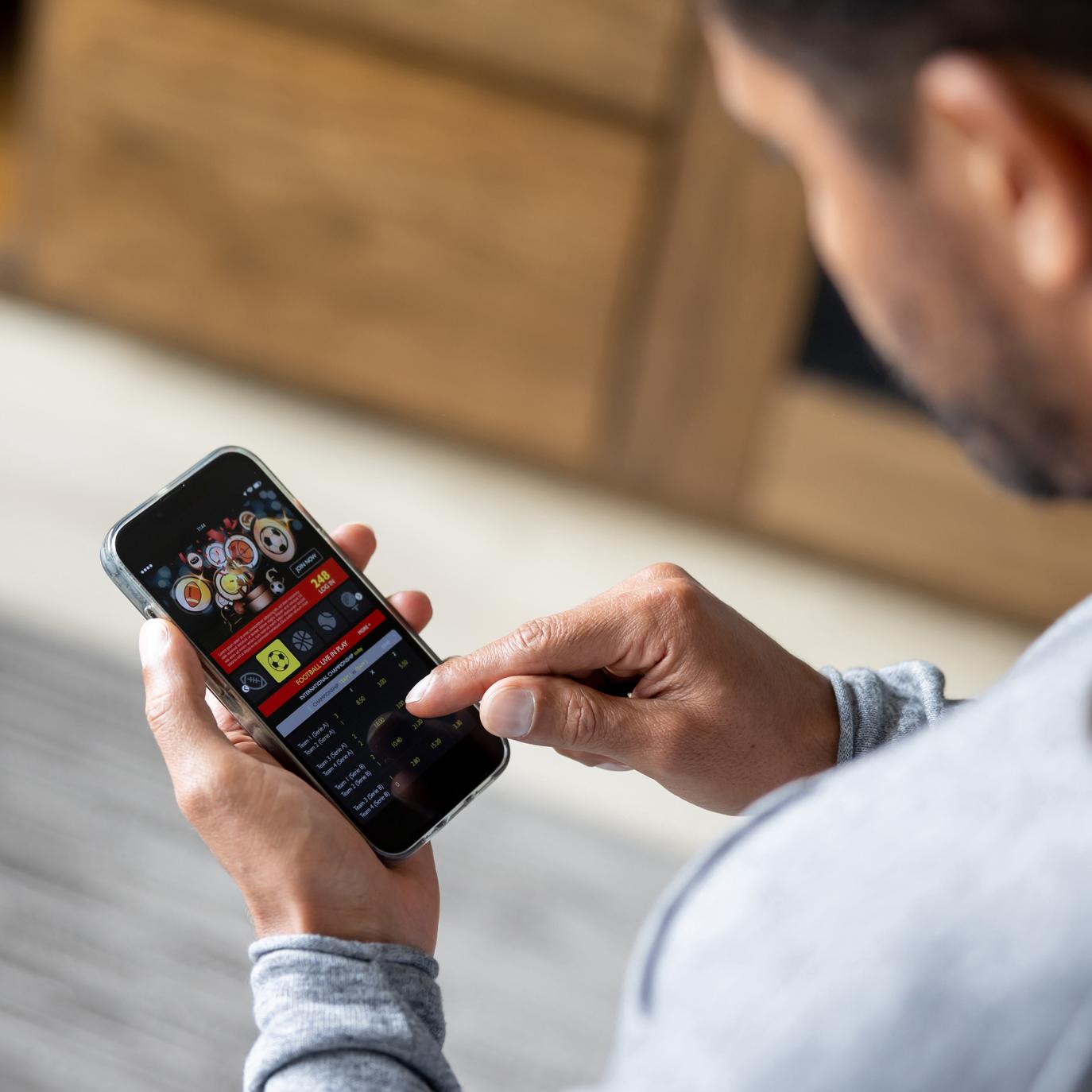 Ein Mann schaut auf sein Handy, auf dem eine Spiele-App geöffnet ist.
