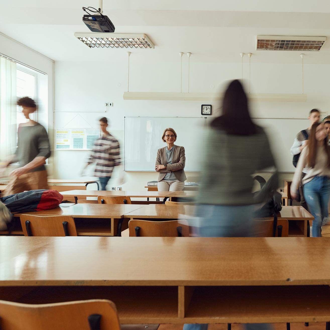 Ein Klassenzimmer mit Schülerinnen und Schülern, die zu ihren Plätzen gehen.
